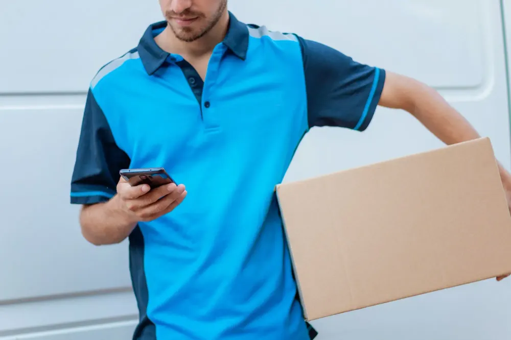 Close up of a man in a blue shirt reading on his phone while delivering a package